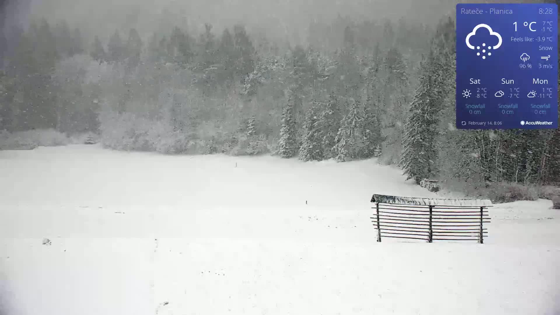 A snow-covered landscape with a wooden fence in the foreground, under heavy snowfall.
