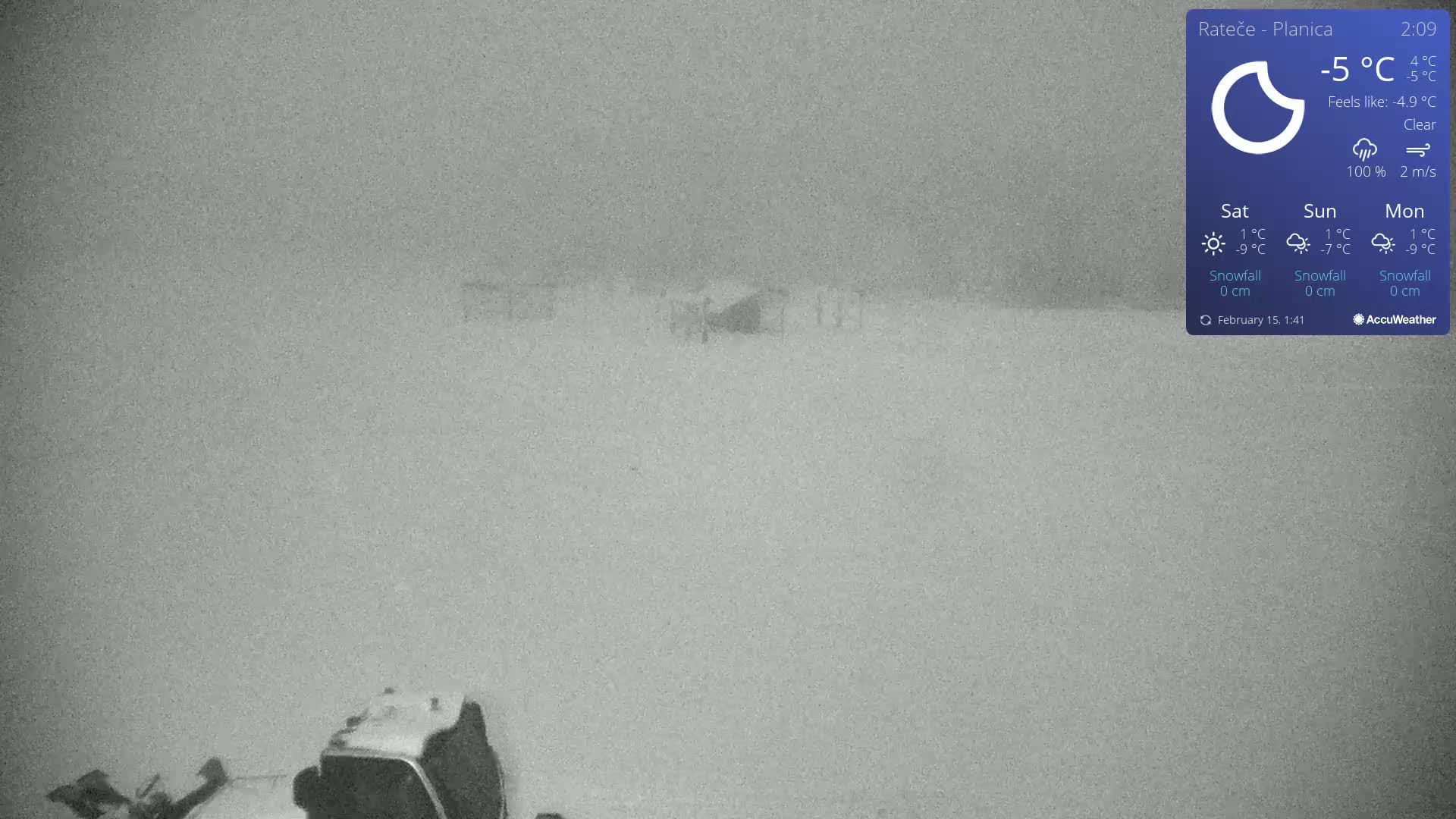 A snow-covered landscape with a vehicle partially visible in the lower portion of the image under clear skies and a temperature of -5°C.