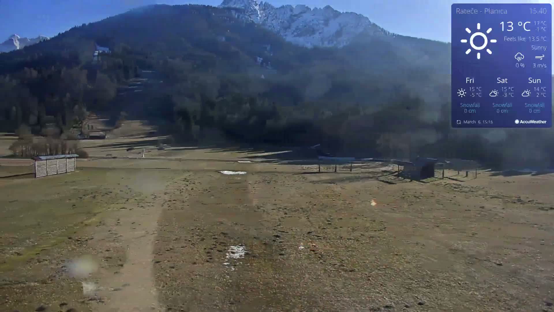 A sunny, mostly barren landscape with a dirt path stretches towards snow-capped mountains under a clear blue sky.