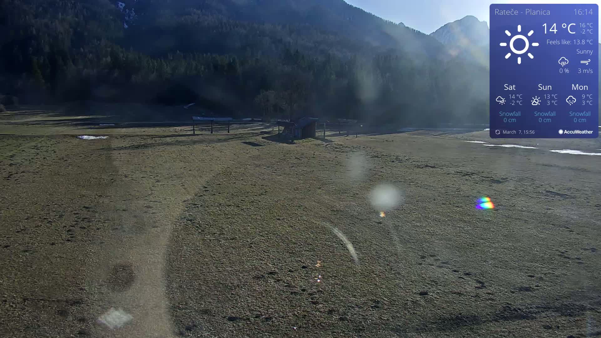 A sunny, flat, brown field with a small shed and distant mountains under a clear sky.