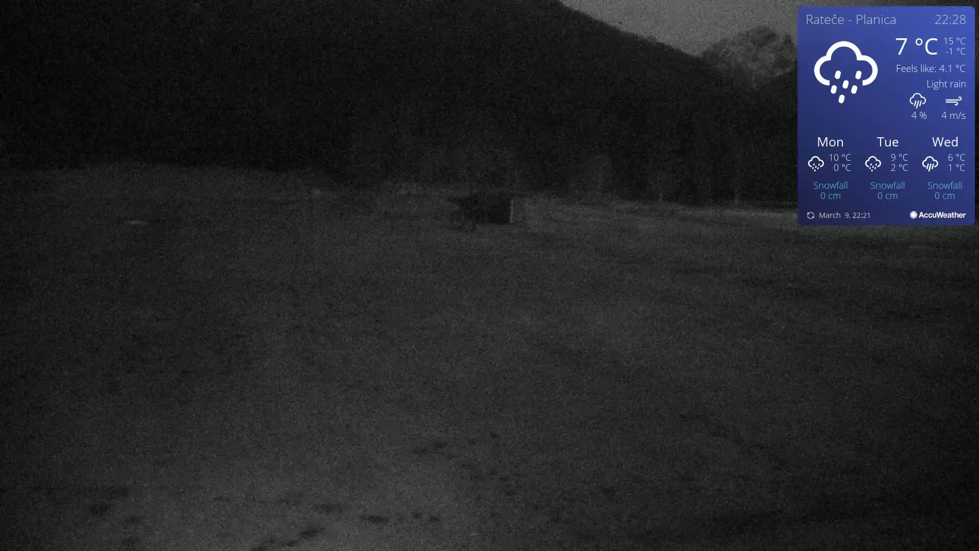 A dark, nighttime outdoor scene shows a mostly empty, flat, dark-colored field under light rain.