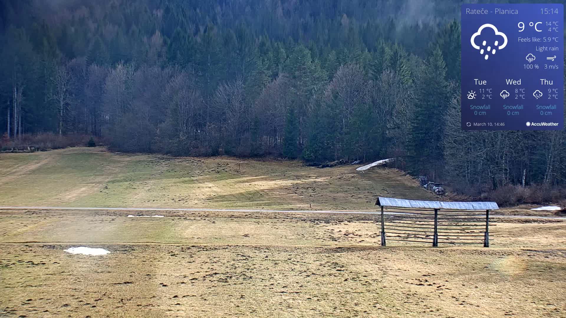 A light rain falls on a flat, grassy field with a wooden structure in the foreground and a dark forest in the background.