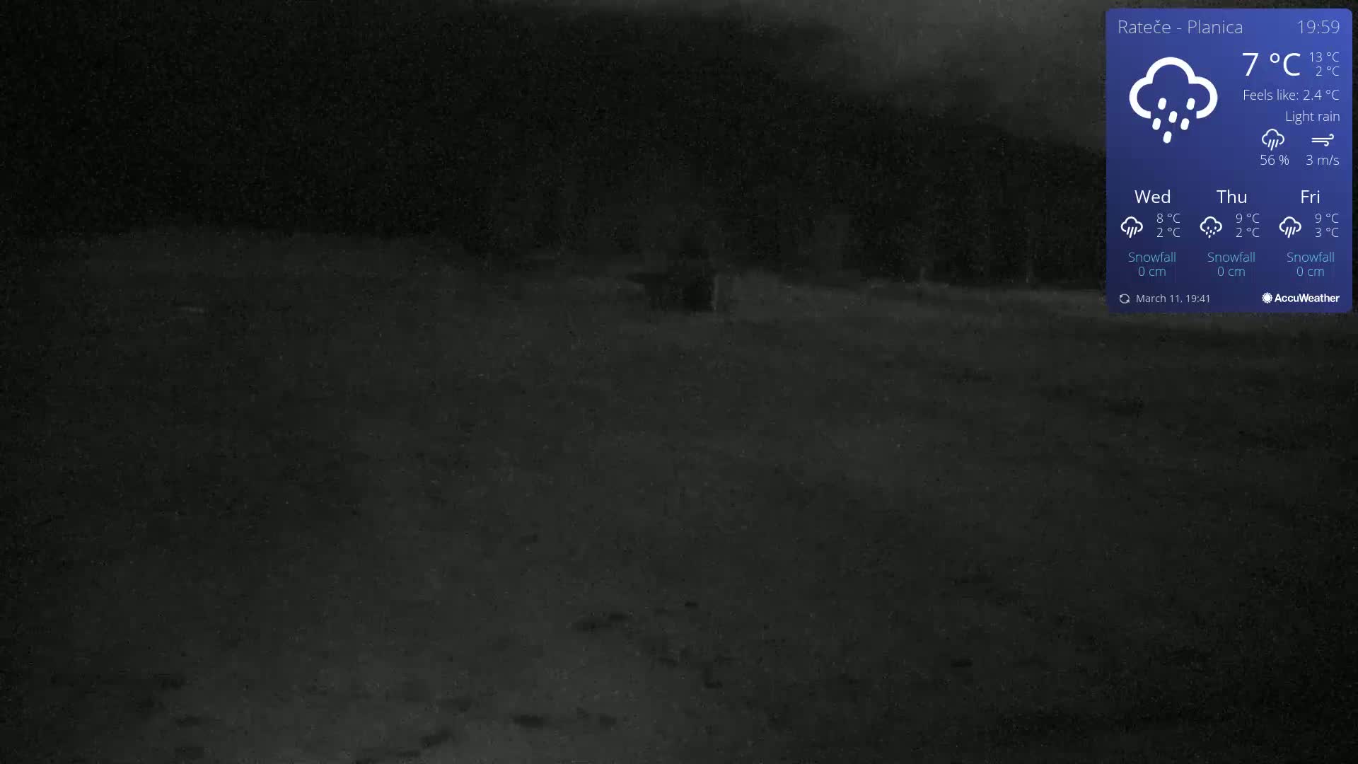 A dark, nighttime outdoor scene of a mostly empty paved area under light rain.
