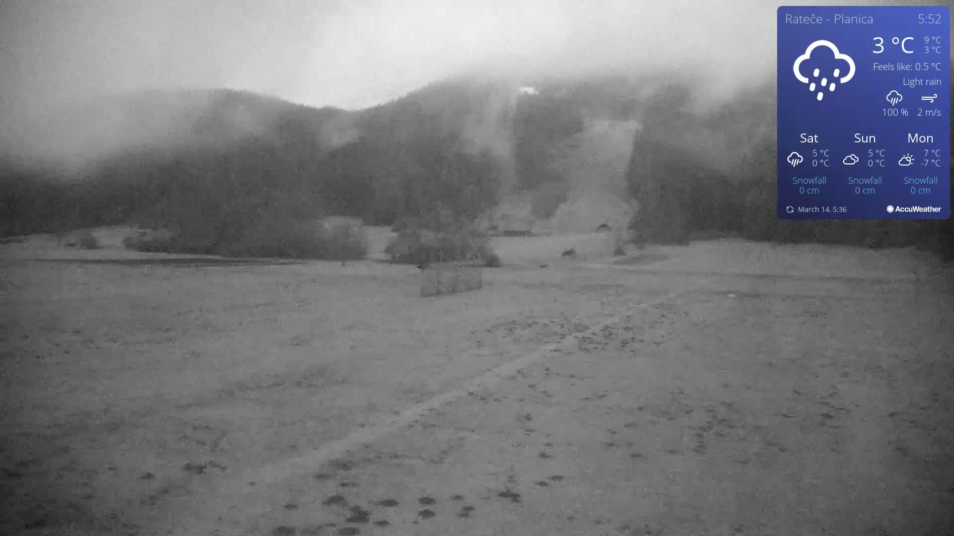 A flat, light-colored landscape stretches out under a gray sky with light rain, toward misty, dark mountains in the background.