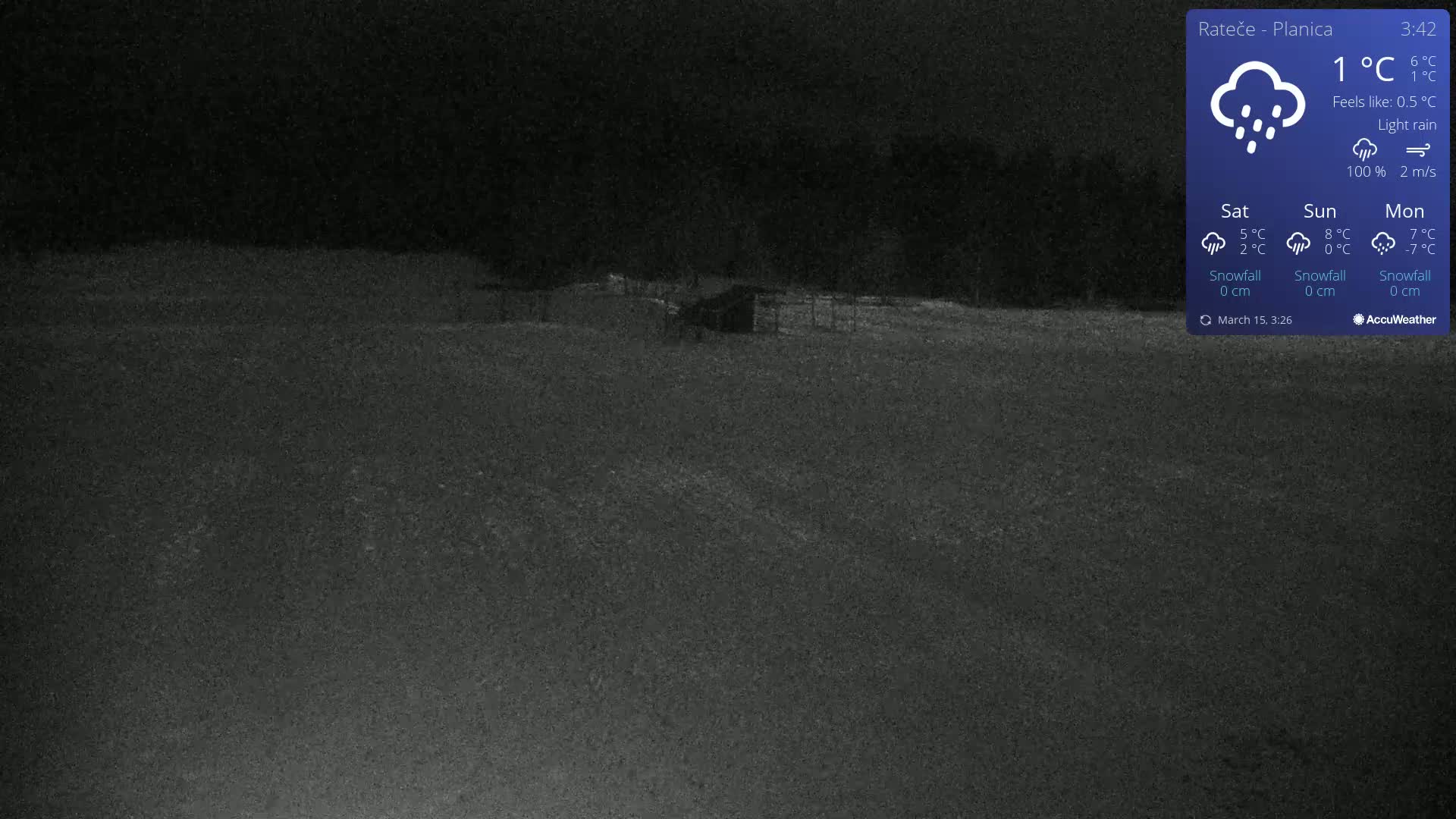 A dark, nighttime view of a flat, snow-covered landscape with a small structure visible in the distance under light rain.