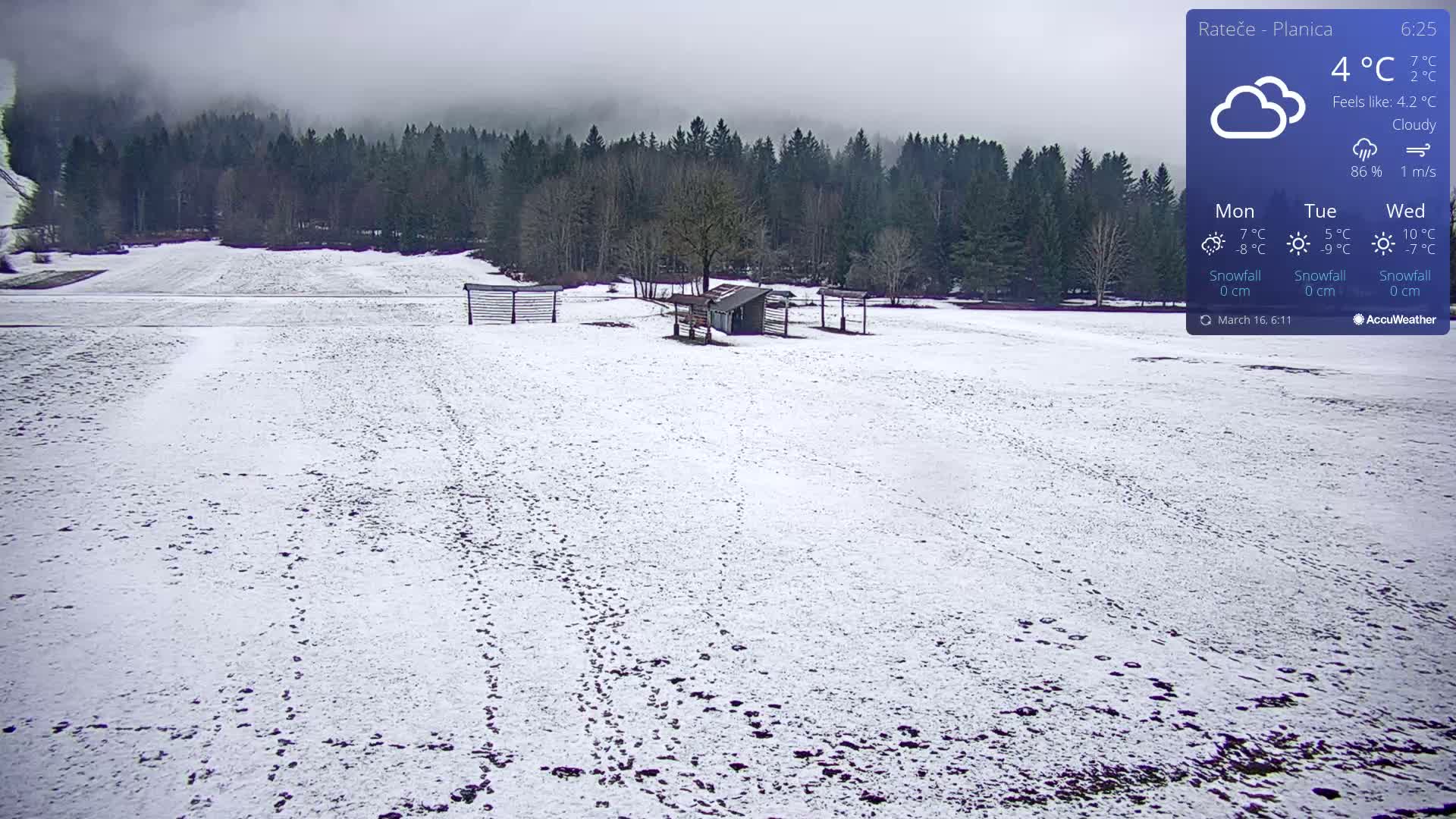 A snow-covered field with footprints, a small shed, and wooden fences is seen under cloudy skies.