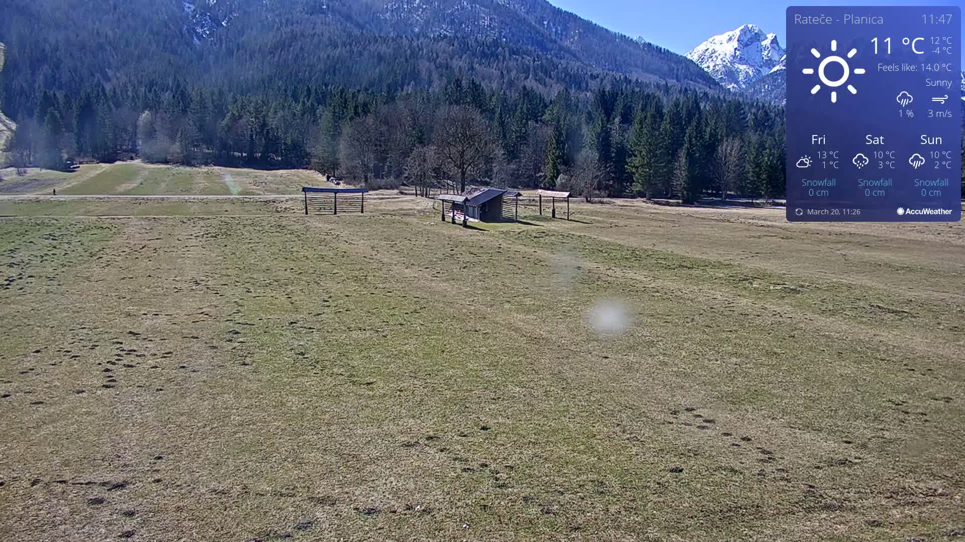 A sunny day shows a grassy field with a small structure and distant mountains, under a mostly clear sky.