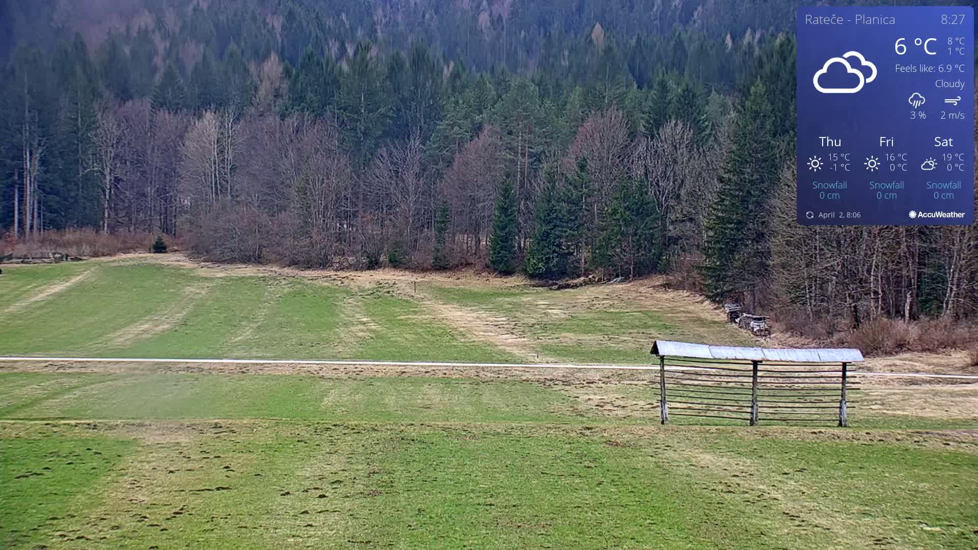 A cloudy day reveals a grassy field with a wooden structure in the foreground and a forest in the background.