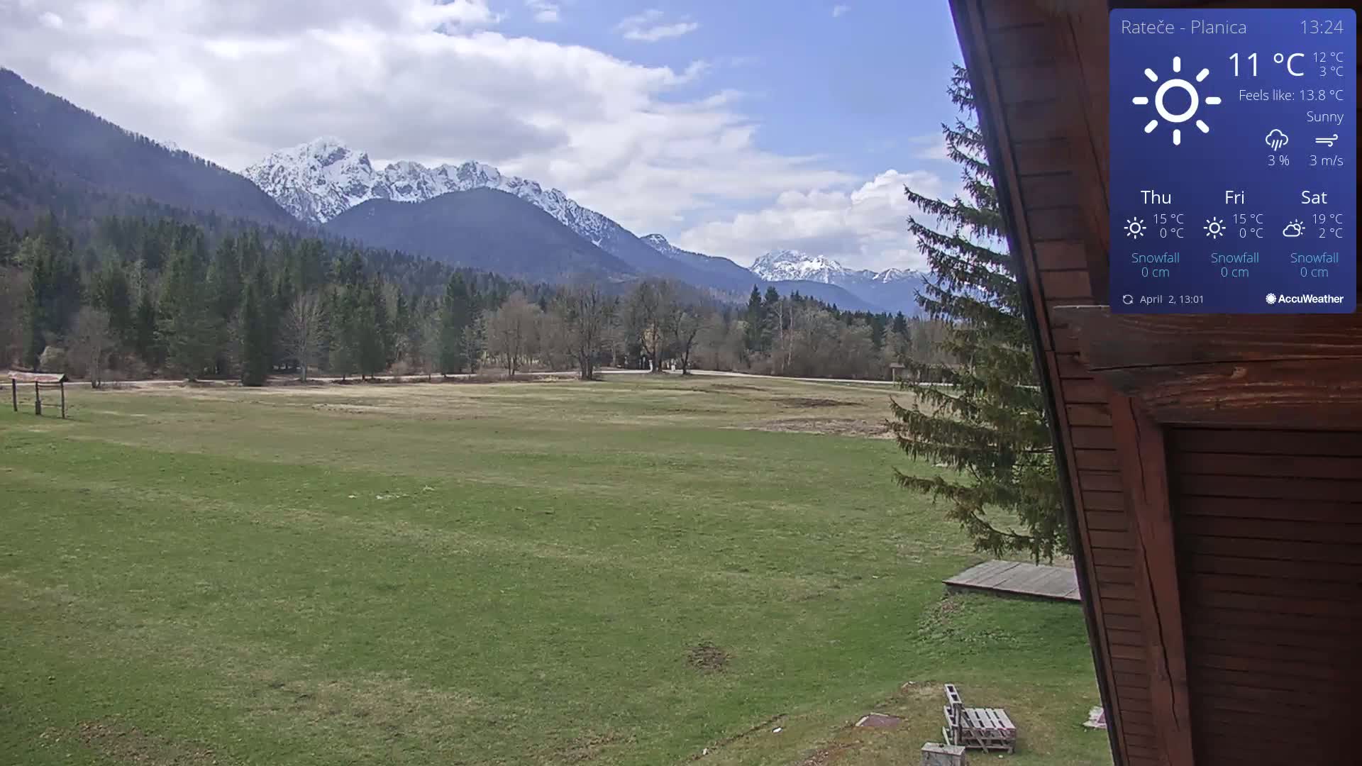 A sunny, partly cloudy day reveals a grassy field with snow-capped mountains in the background.