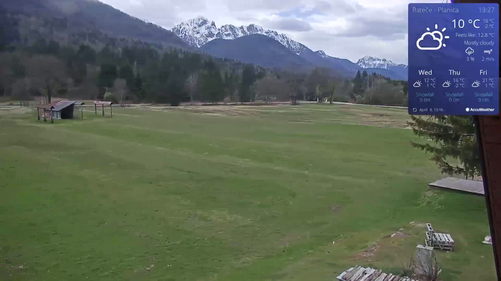 A mostly cloudy day with a temperature of 10°C shows a green field with a small shed and distant snow-capped mountains.