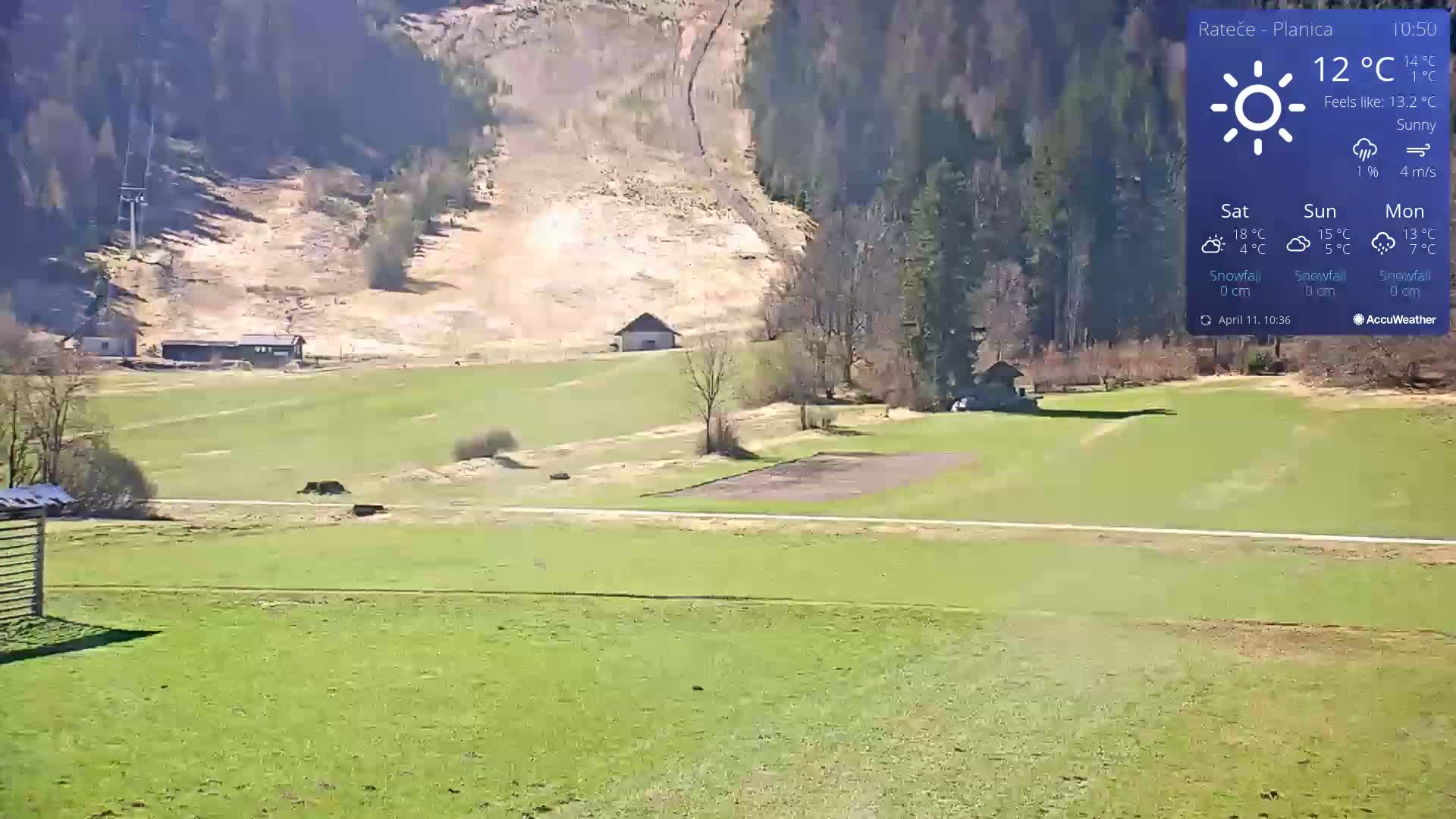 A sunny, green valley with a few buildings and a ski lift in the background, under a clear sky.