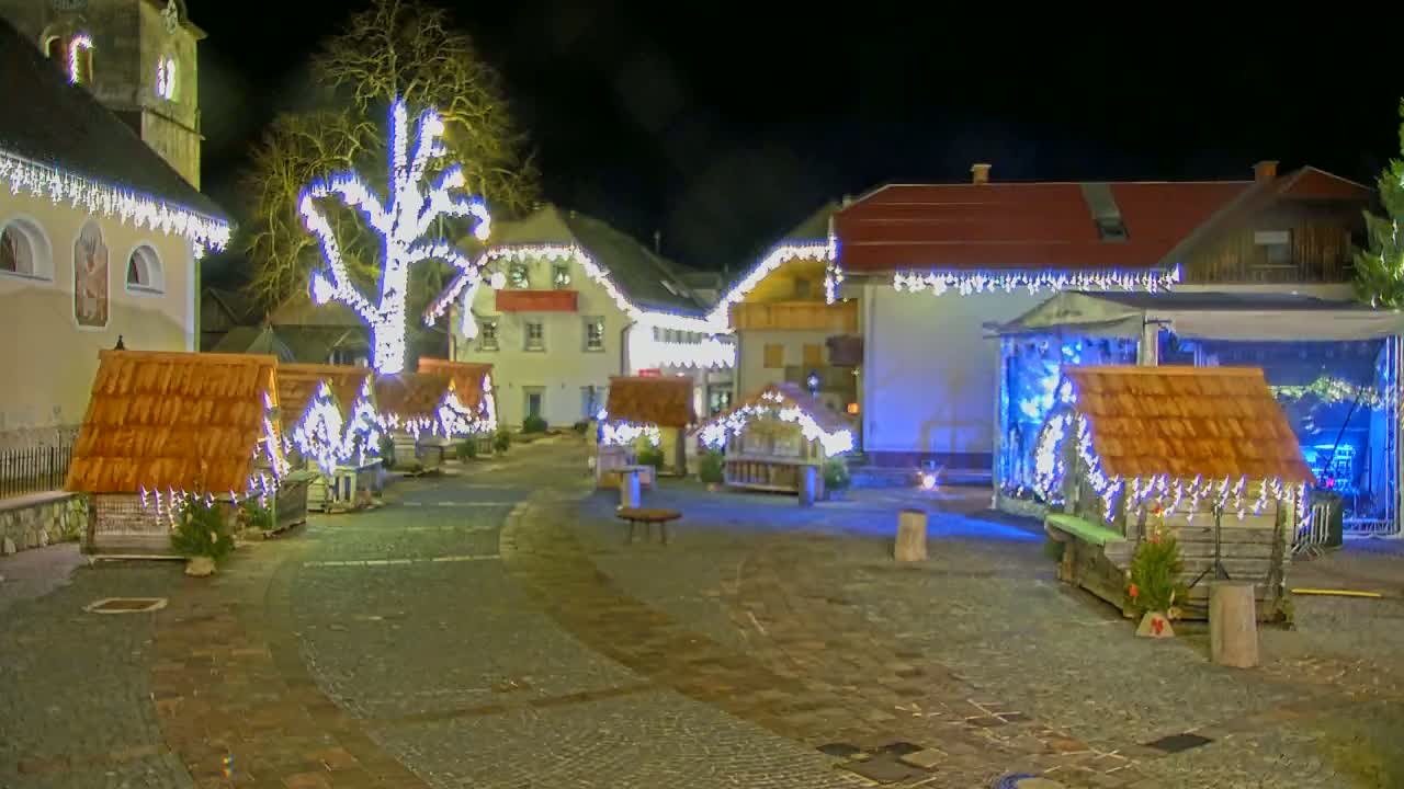 A nighttime scene of a town square decorated with small wooden huts and string lights, illuminated under a dark sky.