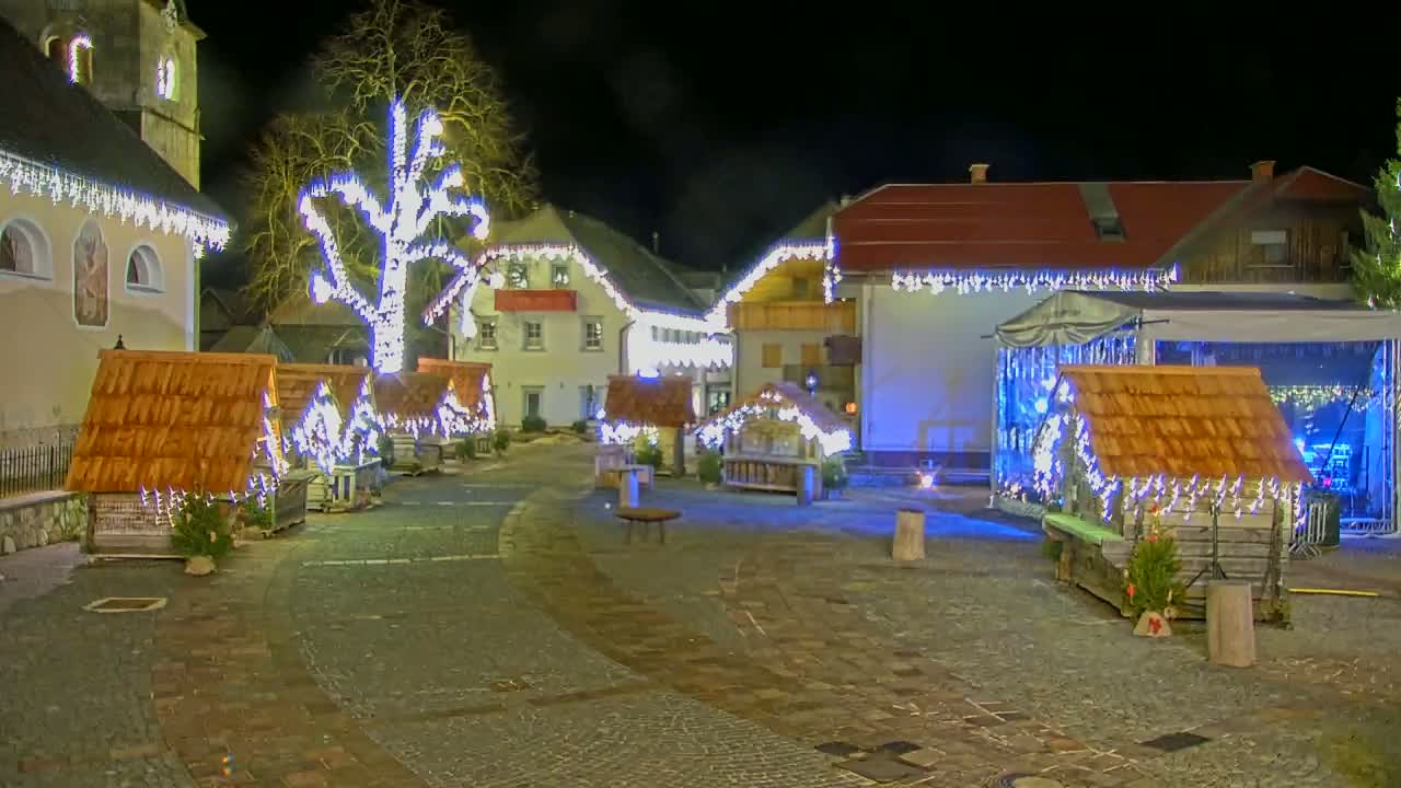 A nighttime village square is decorated with small wooden structures and string lights, illuminated against a dark sky.