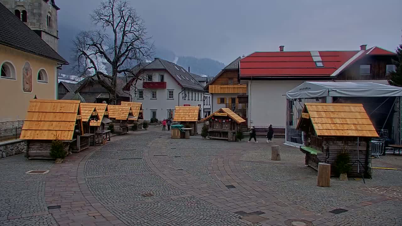A town square with several small wooden stalls, surrounded by buildings under an overcast sky.