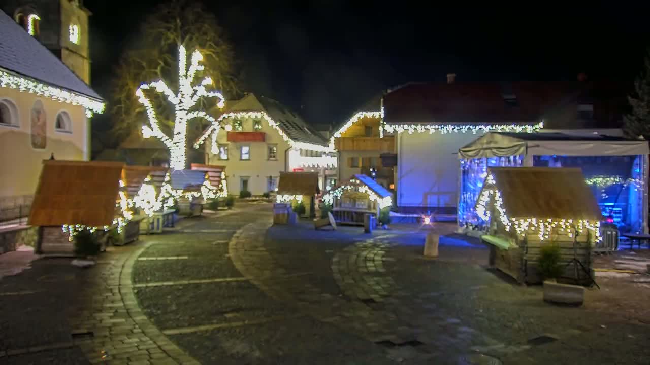 A nighttime scene of a village square decorated with Christmas lights on buildings and small wooden huts.