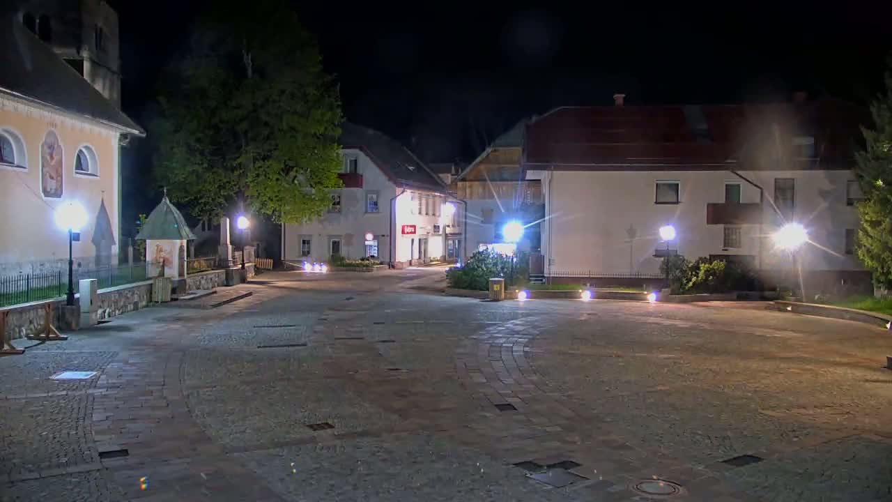 An empty town square at night, illuminated by streetlights, is surrounded by buildings, including a church.