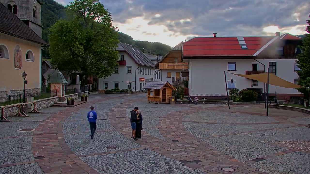 A cobblestone town square with several buildings, including a church, under a cloudy sky.