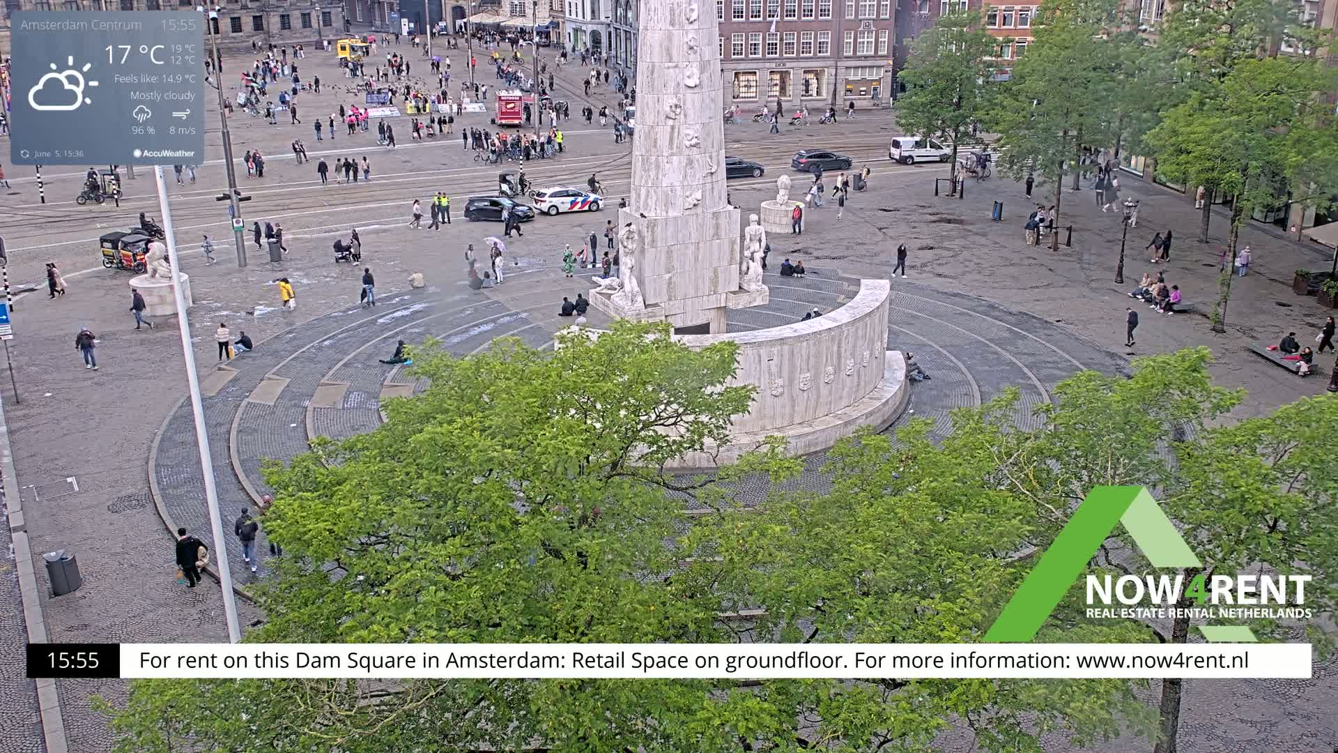 A mostly cloudy day shows a large stone monument in a square with people walking around and sitting on the steps.