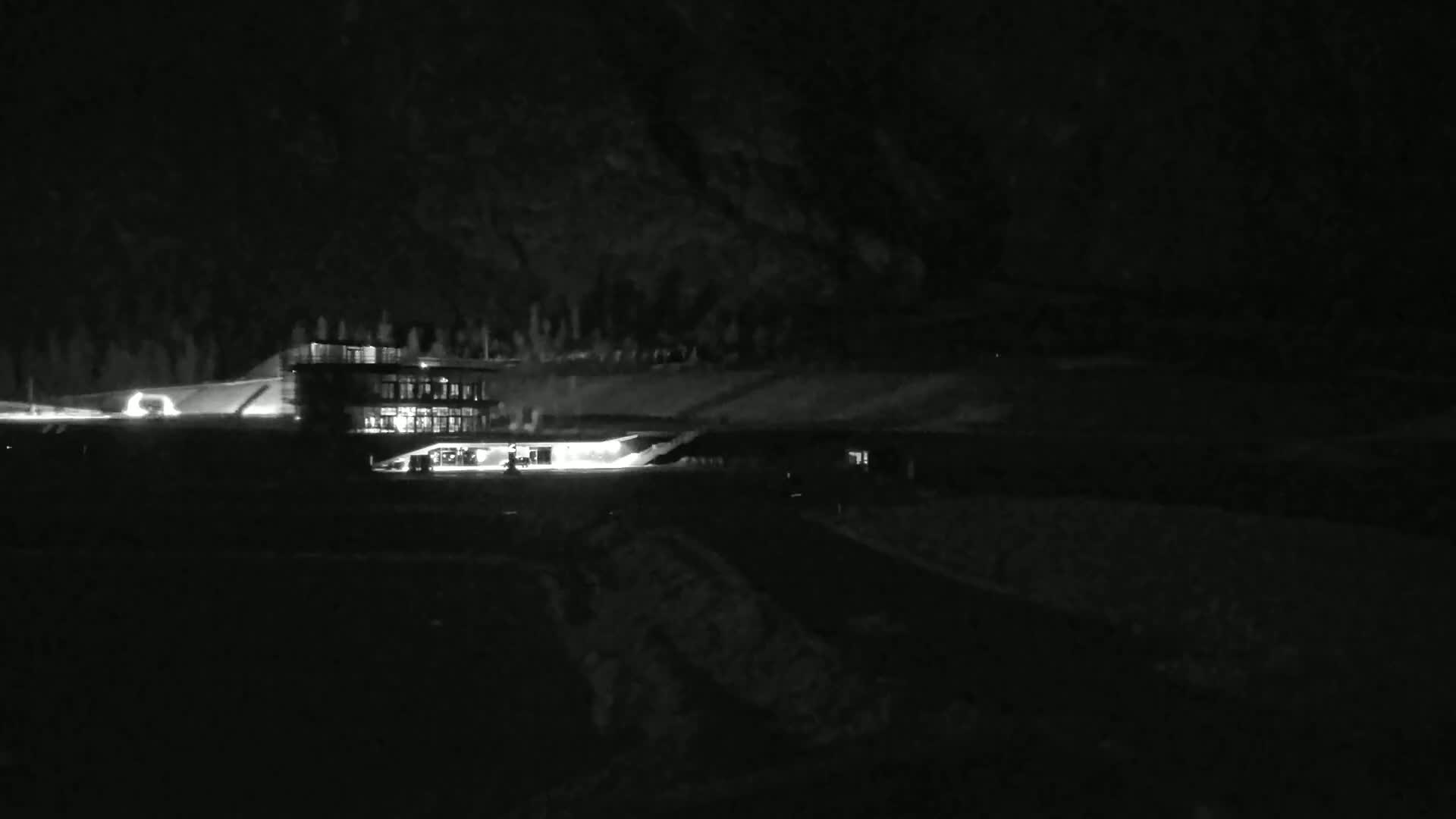 A brightly lit building sits on a dark, hilly landscape at night.