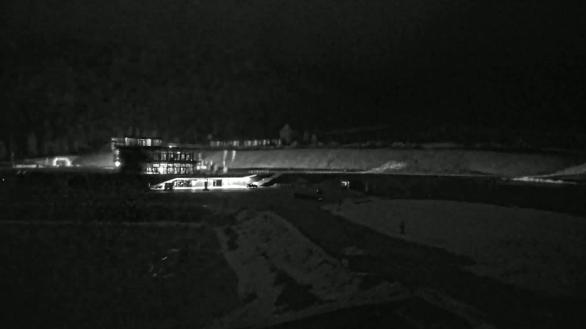 A dimly lit building is visible at night, with a snow-covered landscape surrounding it.
