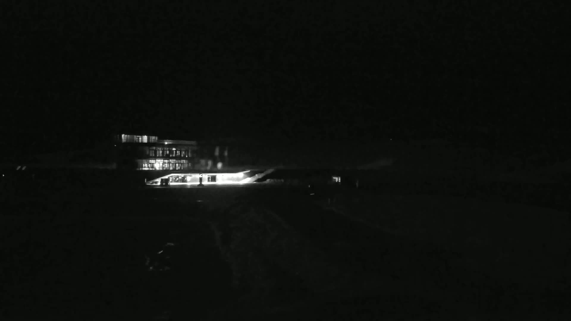 A brightly lit building is visible at night, with a dark, possibly snowy, expanse in front of it.