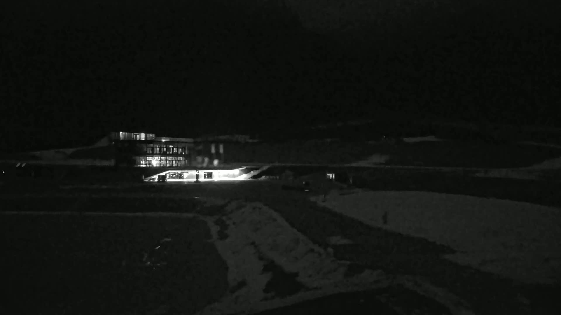 A brightly lit building is visible at night in a snow-covered landscape.