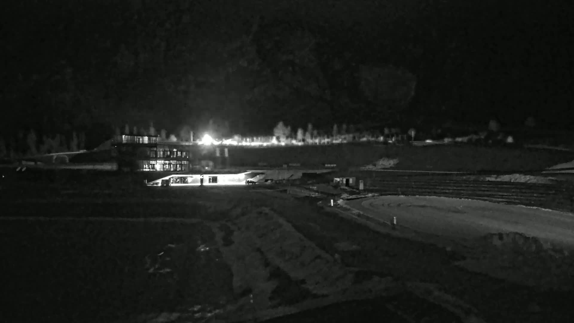A brightly lit building sits near a dark, snow-covered oval track at night.