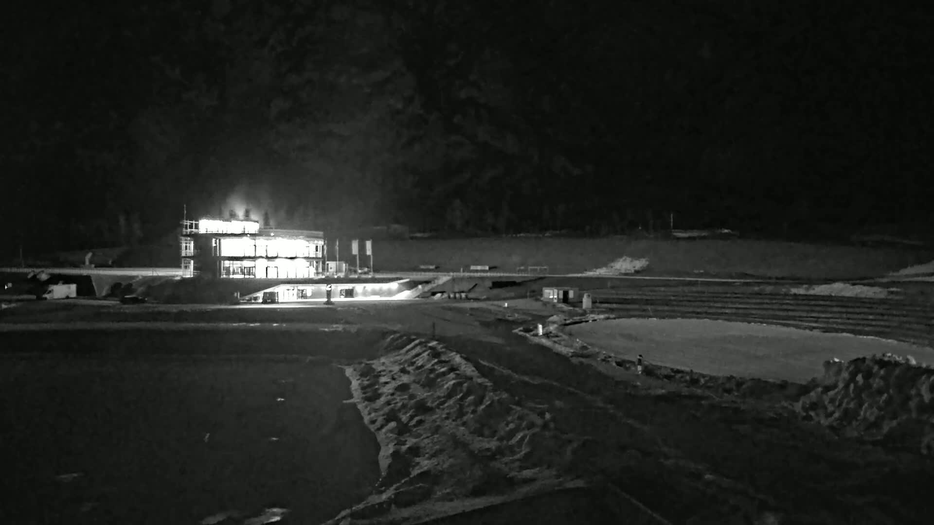 A brightly lit building stands in a dark, snow-covered outdoor area at night.