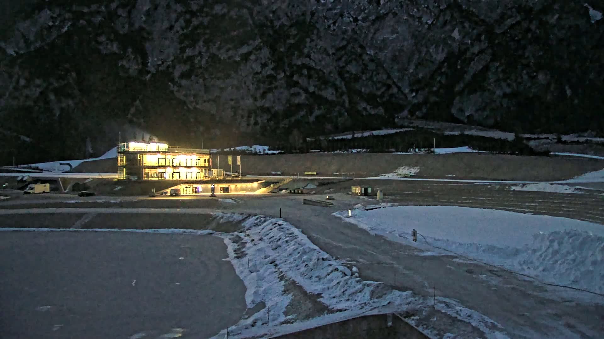 A brightly lit building stands near a snowy, outdoor area at night, with a dark mountain in the background.