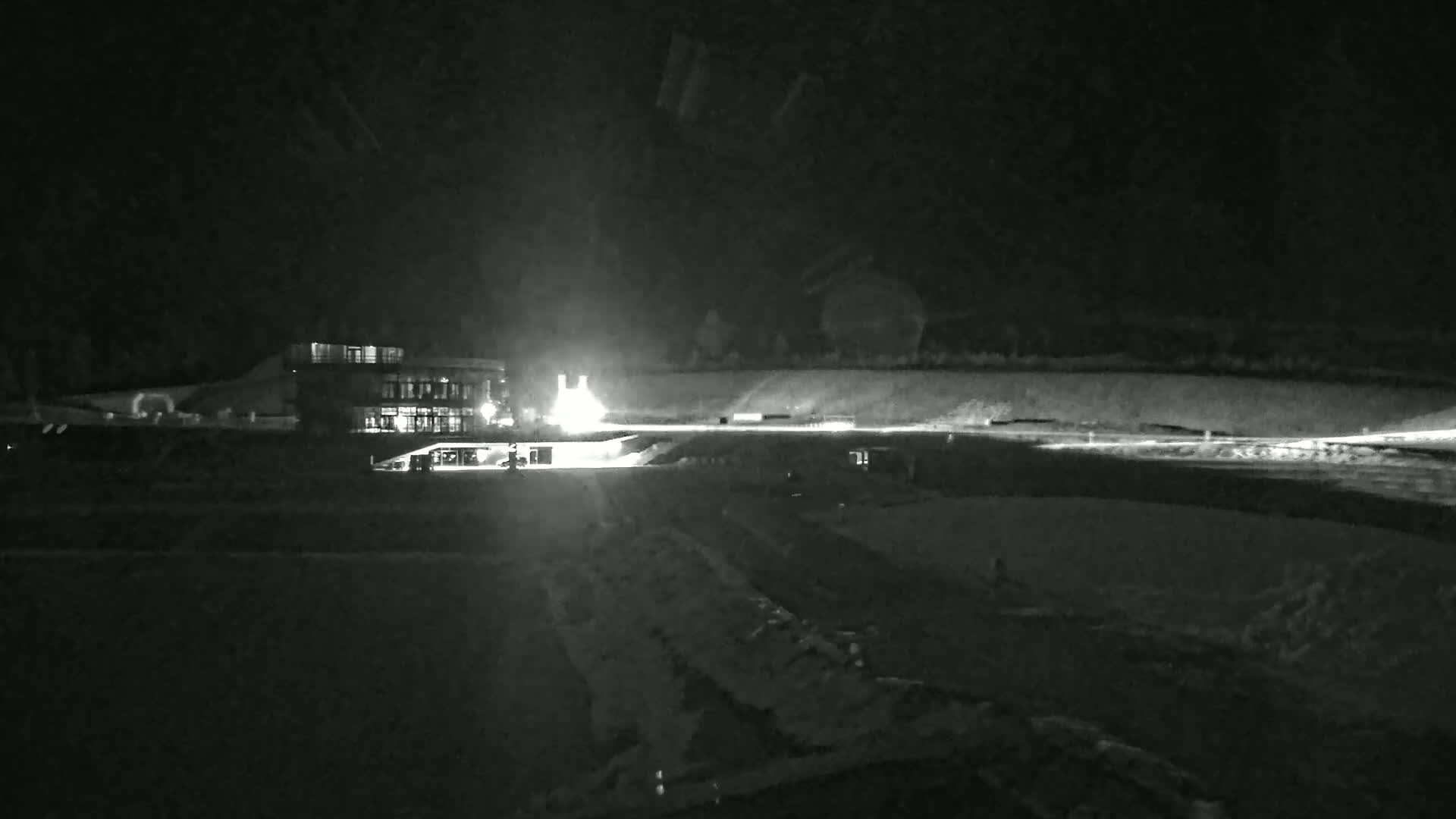 A nighttime, low-light image shows a building illuminated by lights, a road, and a dark, seemingly snowy or icy landscape.