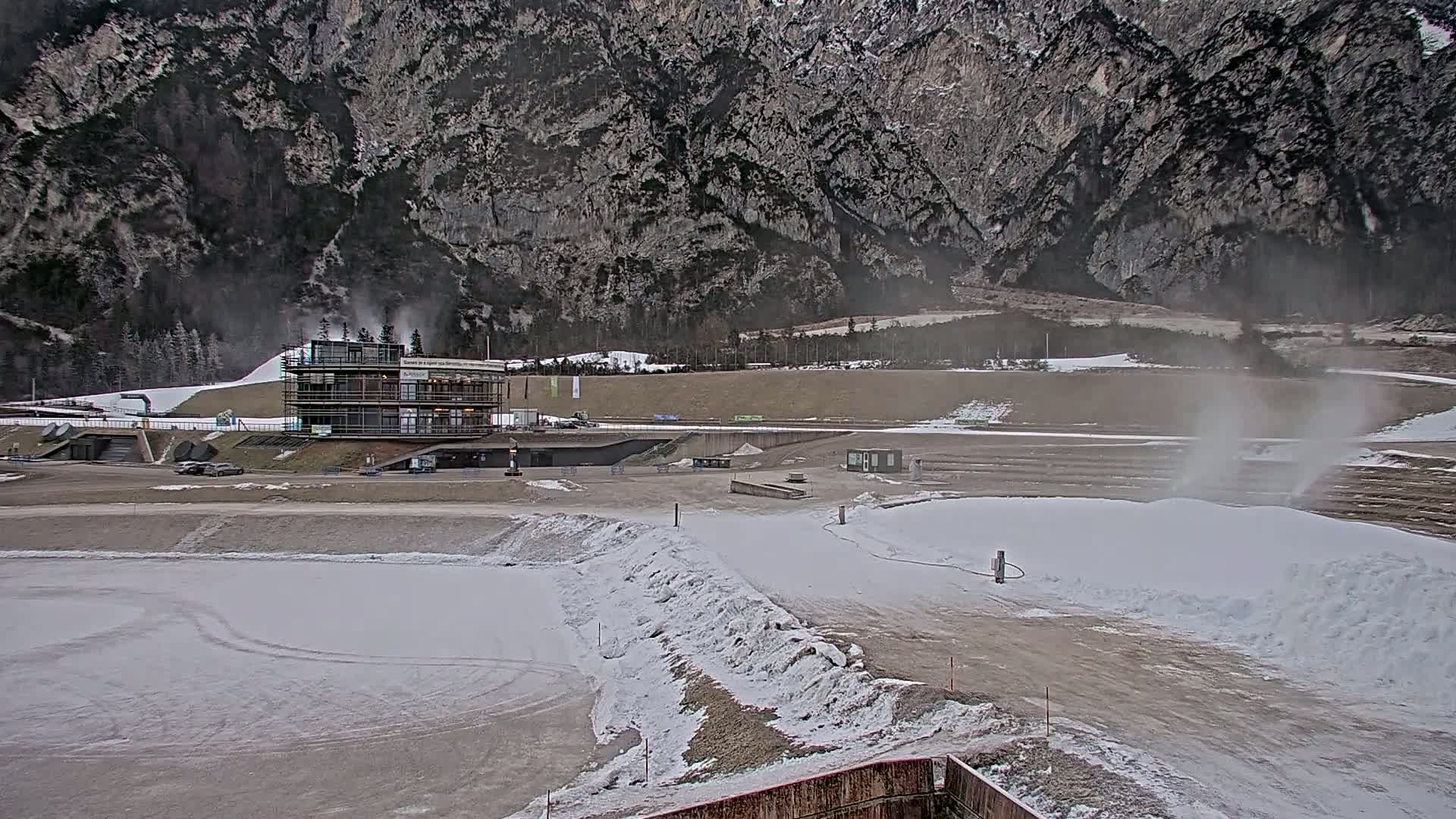 A snowy outdoor sports facility nestled against a mountainous backdrop, with snow cannons operating in the foreground.