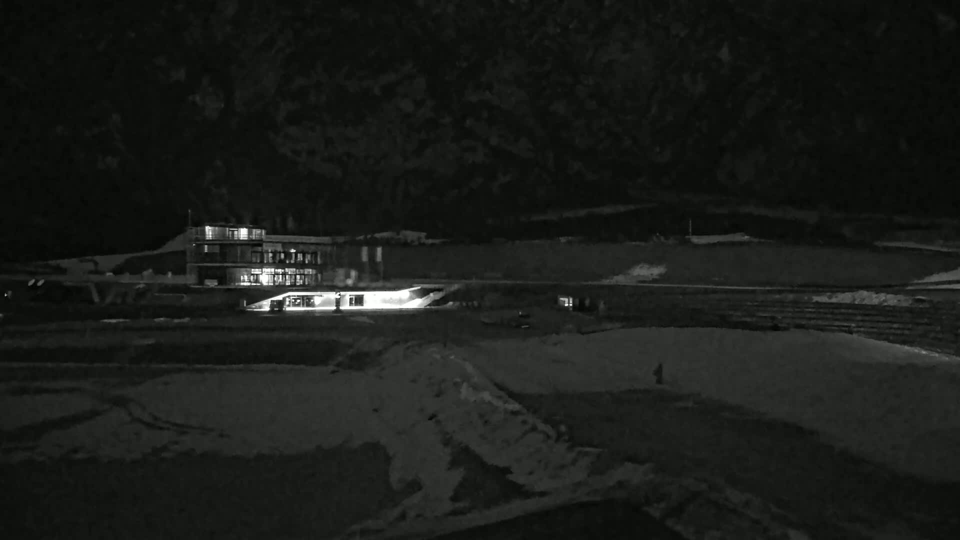 A brightly lit building sits on a snow-covered landscape at night under a dark sky.