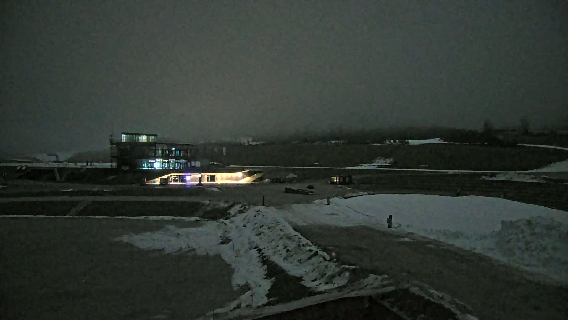A dimly lit, modern building sits on a snow-covered landscape under a dark, overcast sky at night.