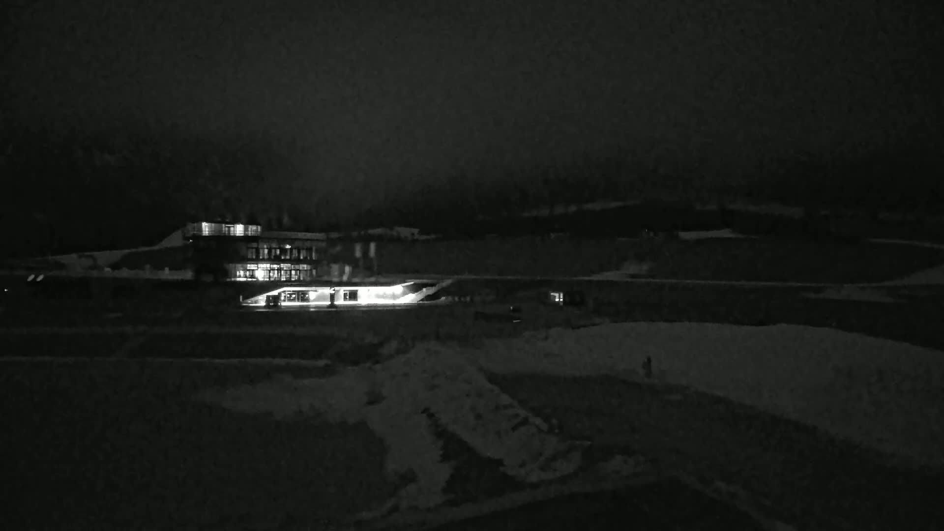 A brightly lit building sits on a snow-covered landscape at night under a dark sky.