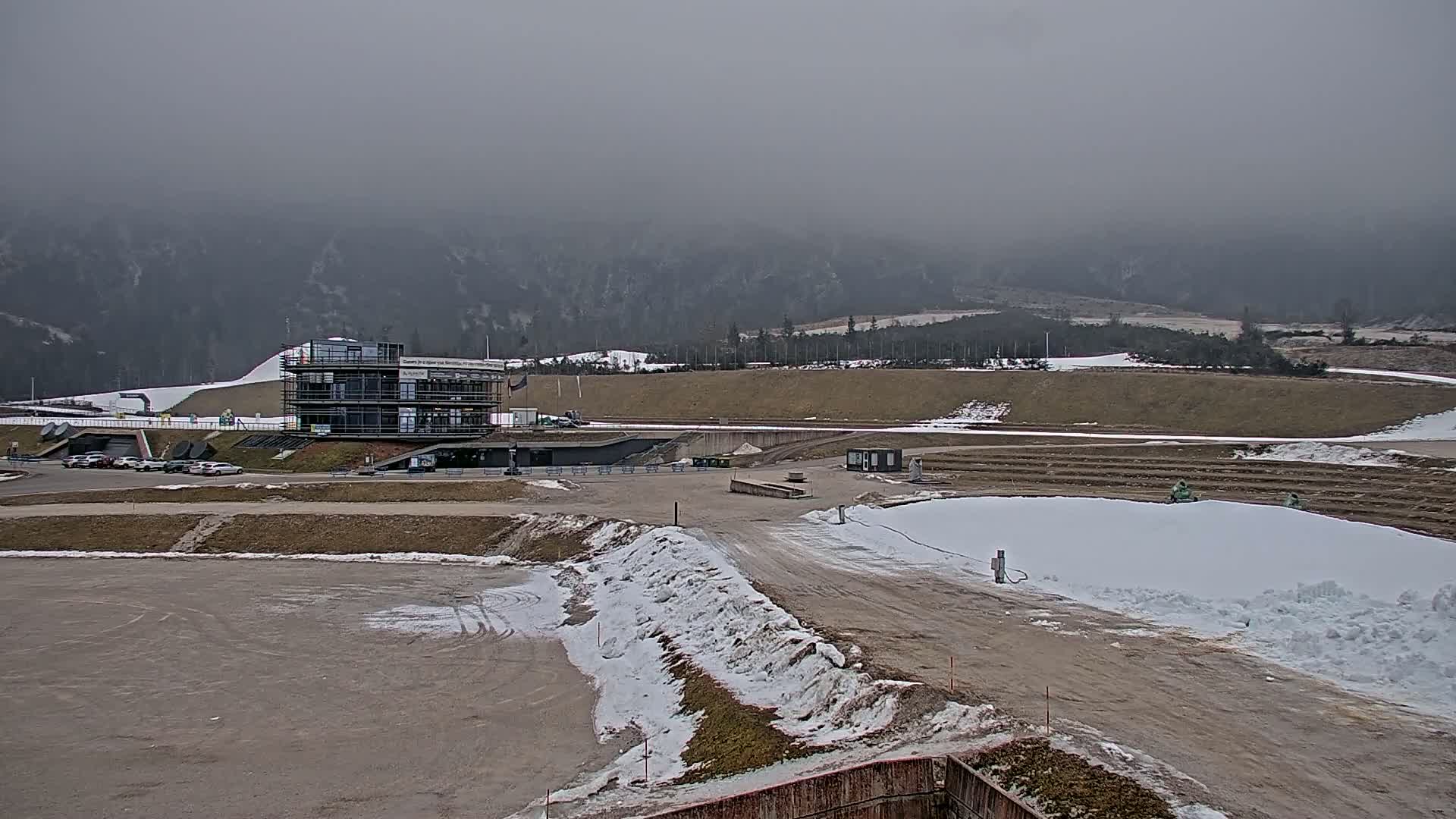 A multi-story building sits in a snow-dusted, mostly barren landscape under a gray, overcast sky, with mountains in the background.