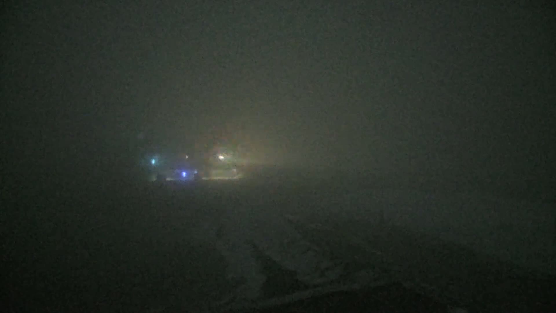 Faintly lit vehicles are barely visible through a thick fog at night.