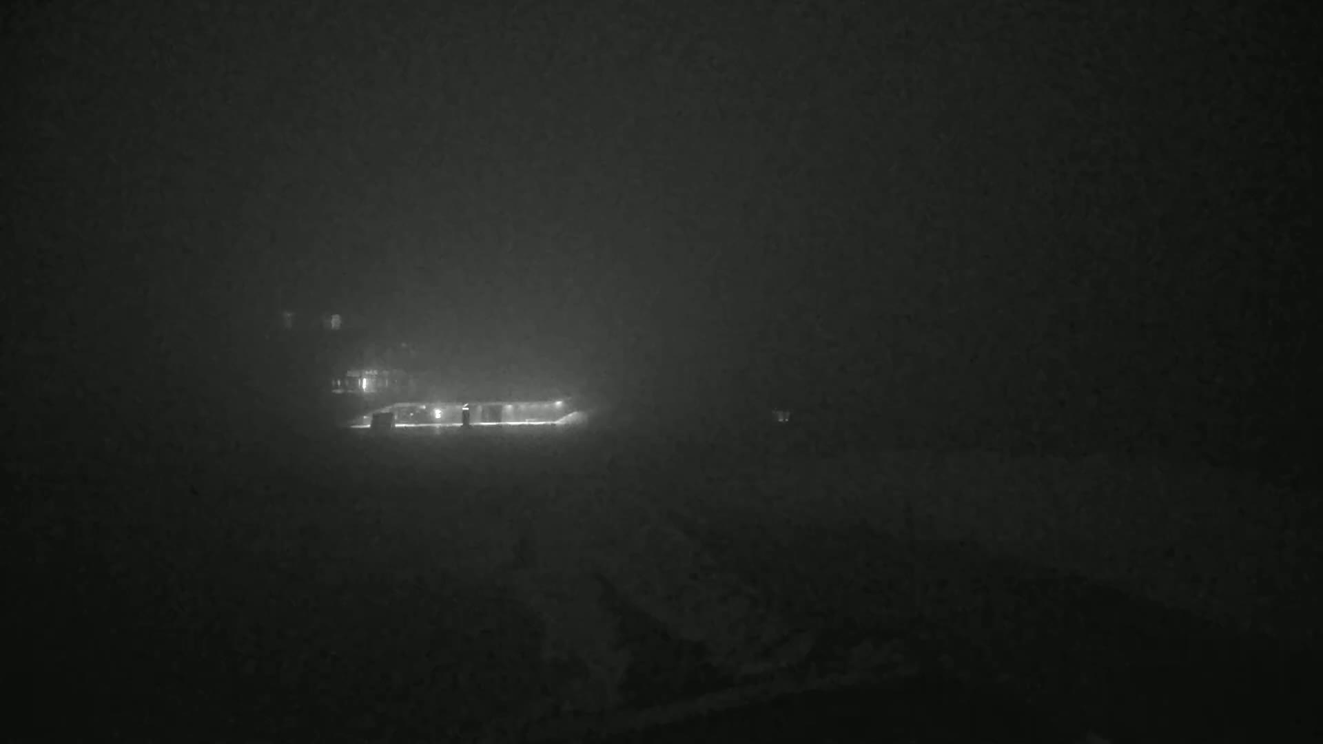 A dimly lit building is barely visible through a thick fog at night.