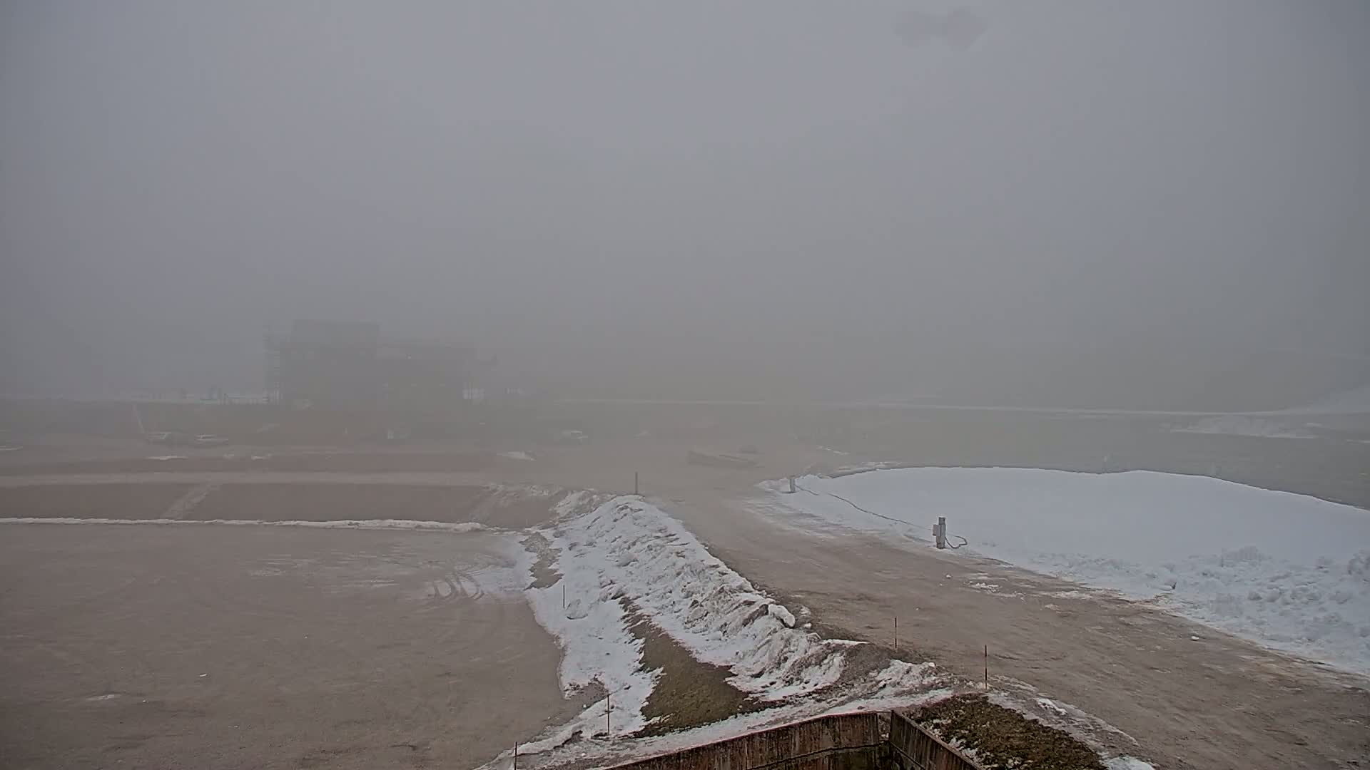 A foggy, snow-dusted construction site with a partially built structure in the distance.
