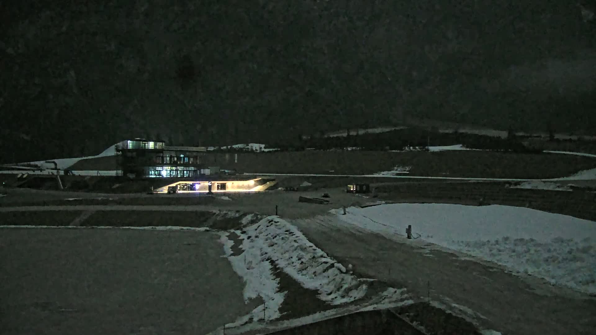 A lit building sits on a snowy, dark landscape under a nighttime sky.
