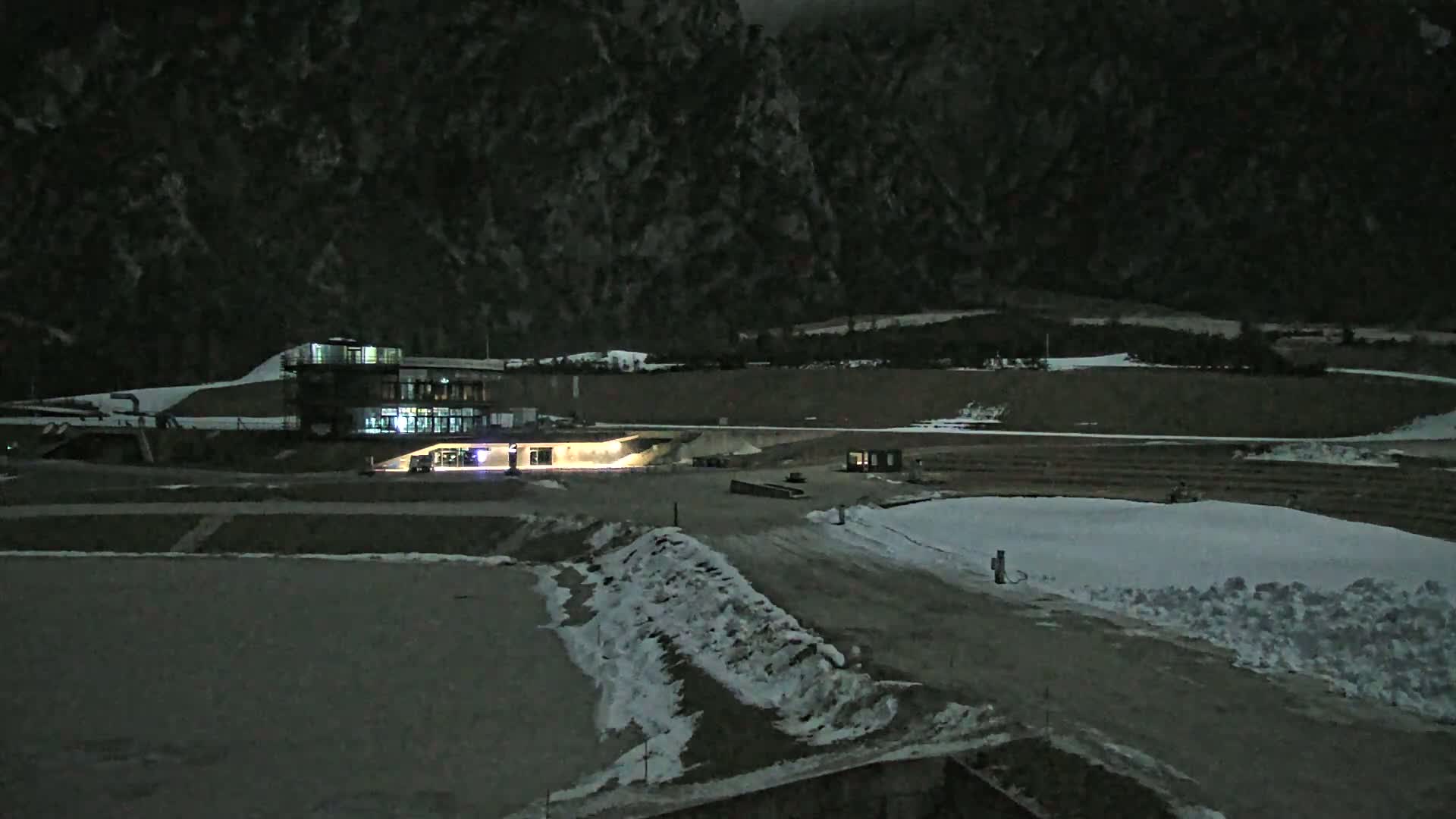 A lit building sits near a snow-covered, dark landscape at night, backed by a mountain range.
