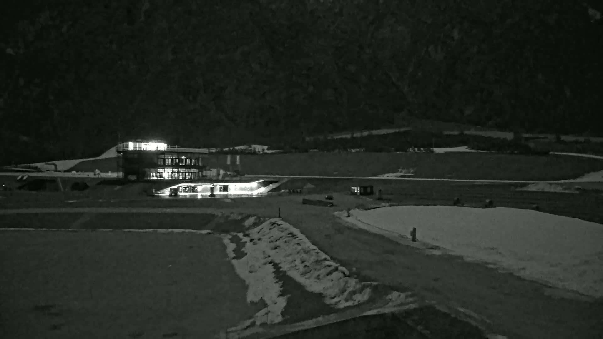 A lit building sits at the base of a dark mountain at night, with patches of snow on the ground.