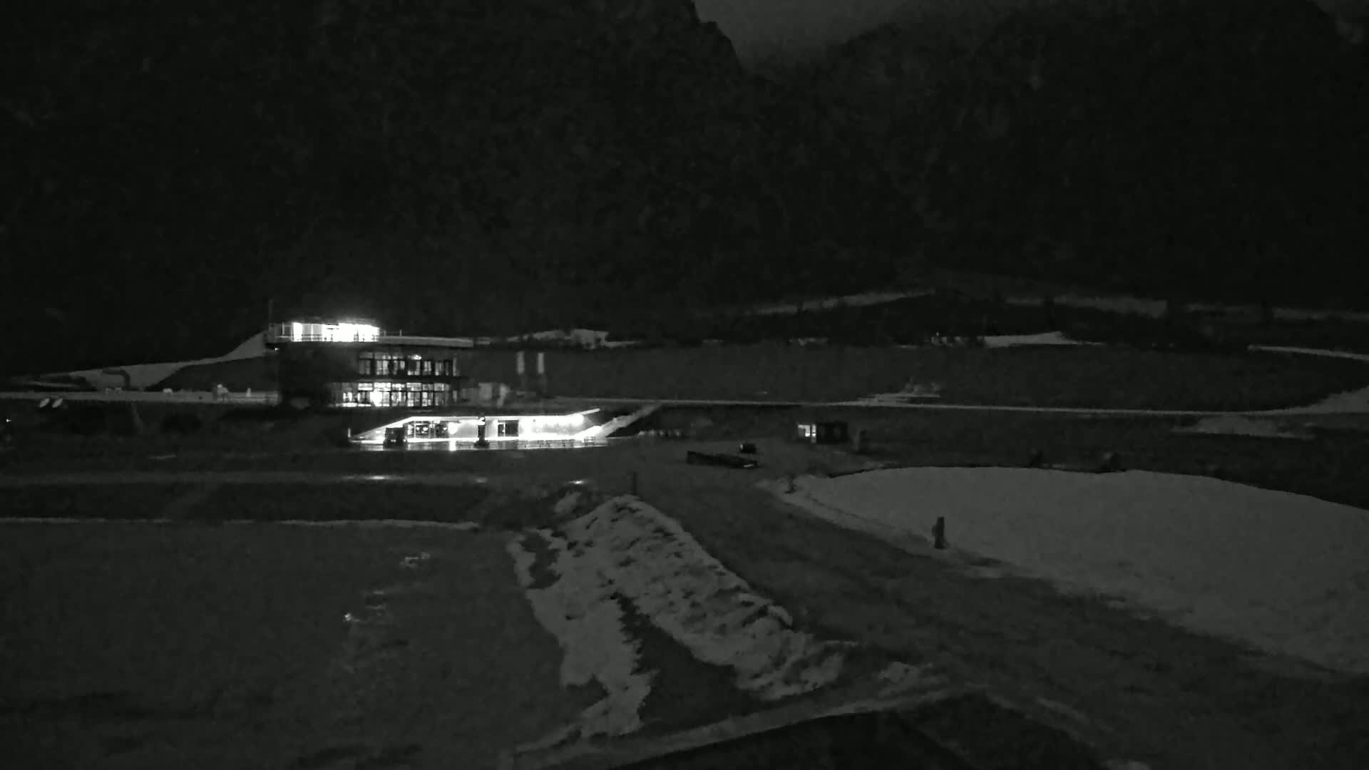 A lit building sits in a snow-dusted, mountainous landscape at night.