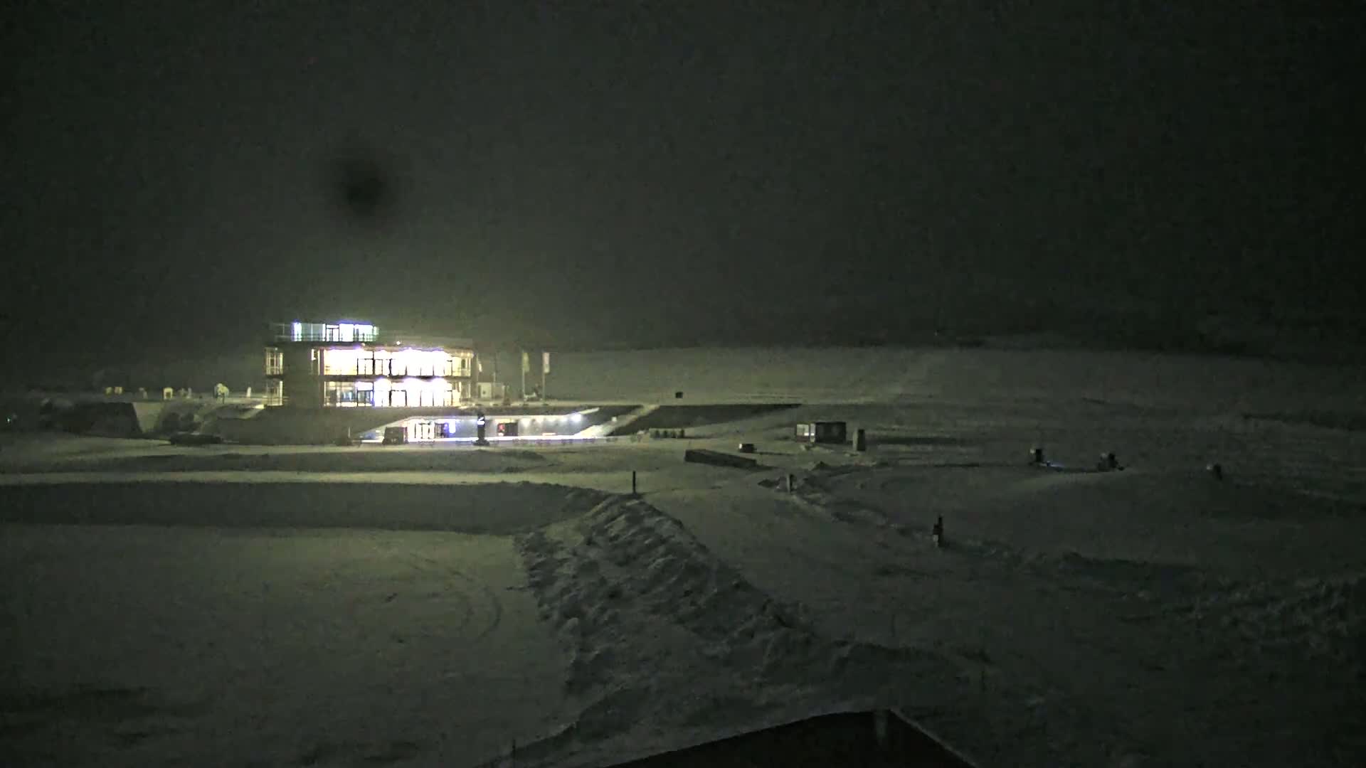 A brightly lit building stands on a snow-covered landscape at night.