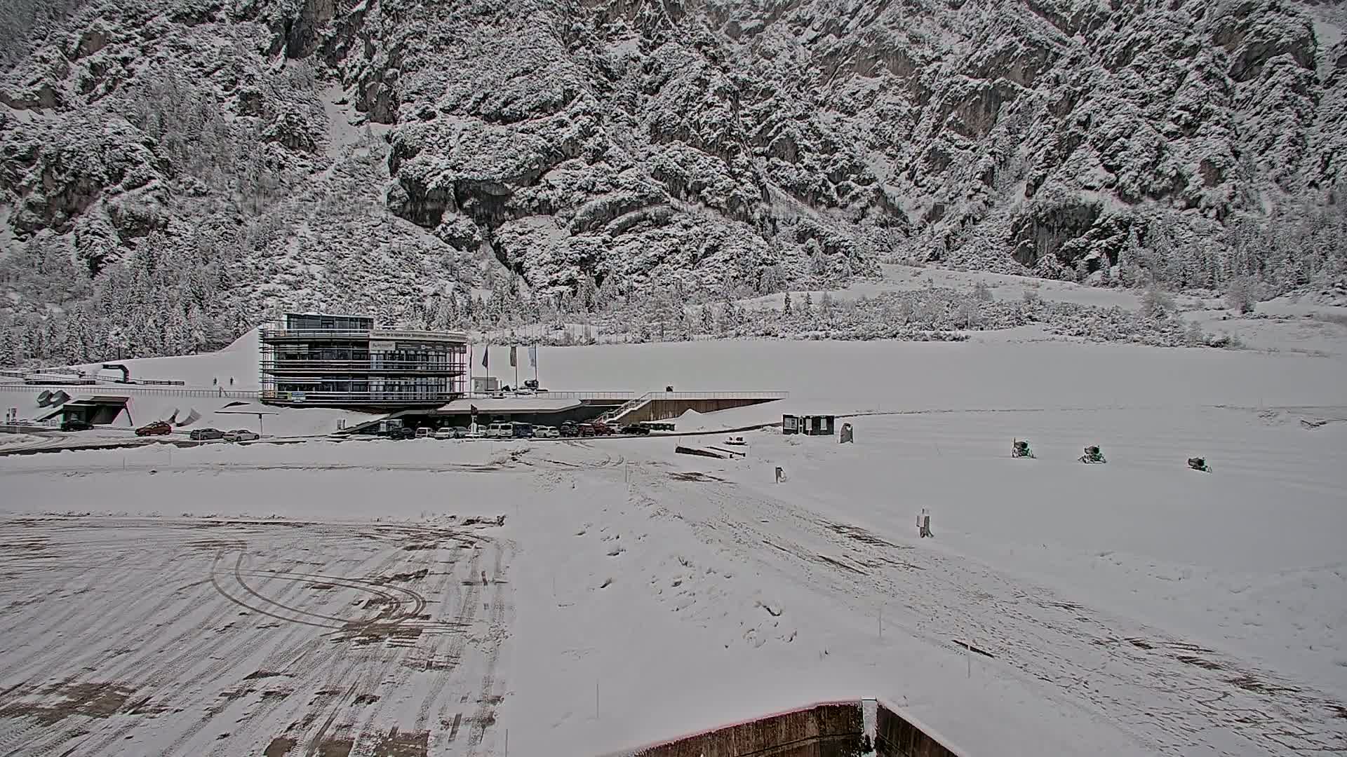 A snow-covered landscape features a modern building near a mountain under a cloudy sky.
