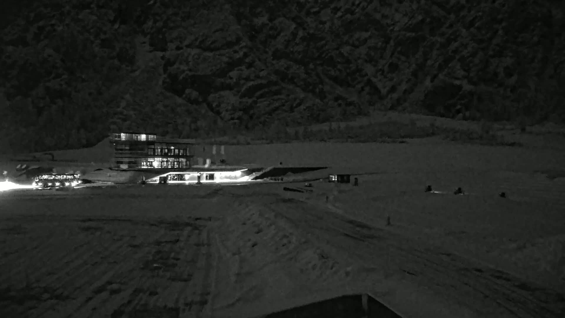 A lit building sits in a snow-covered area at night, with a dark mountainside rising behind it.
