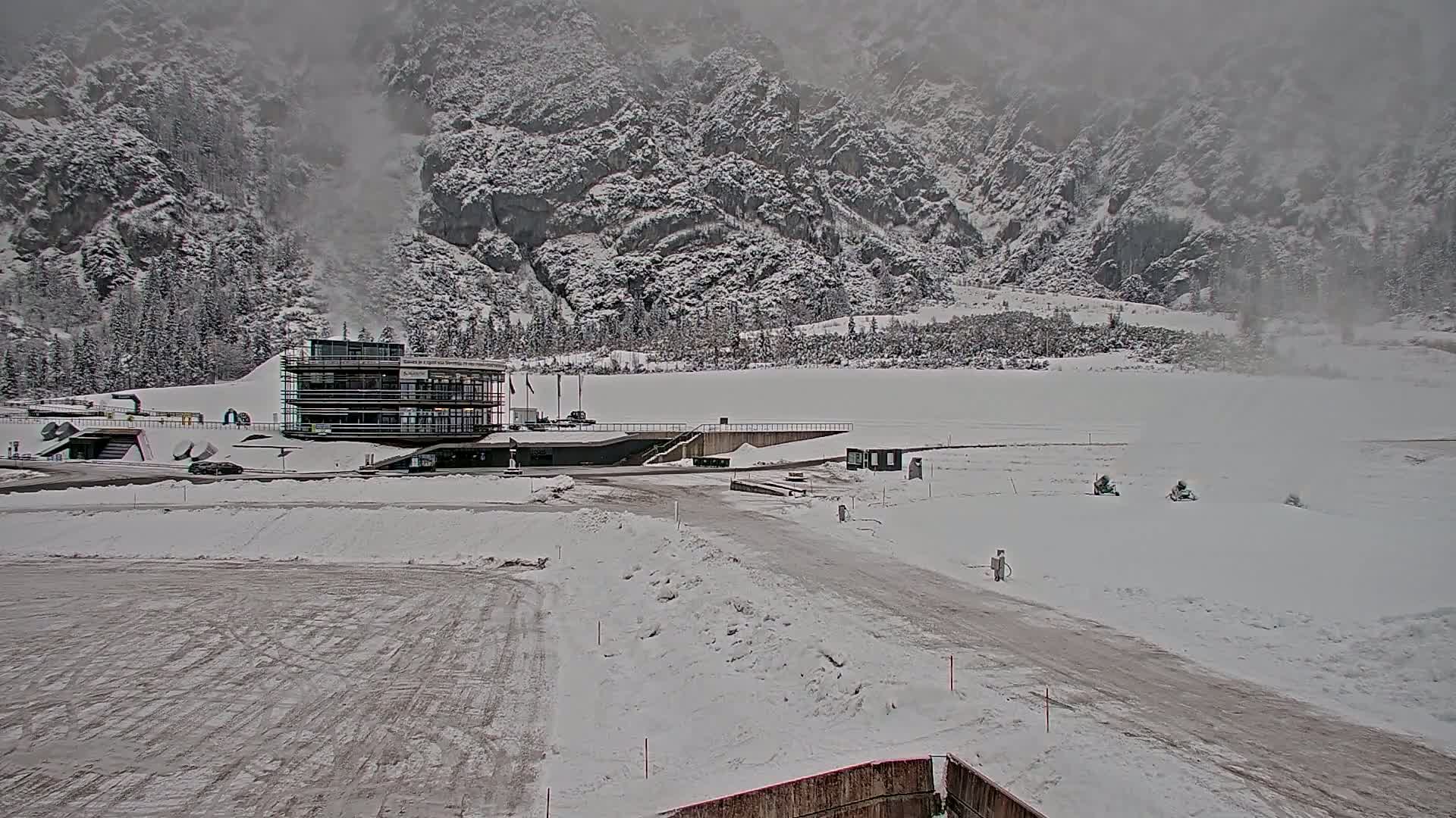 A snow-covered landscape with a modern building and a road, set against a backdrop of snow-covered mountains in foggy weather.