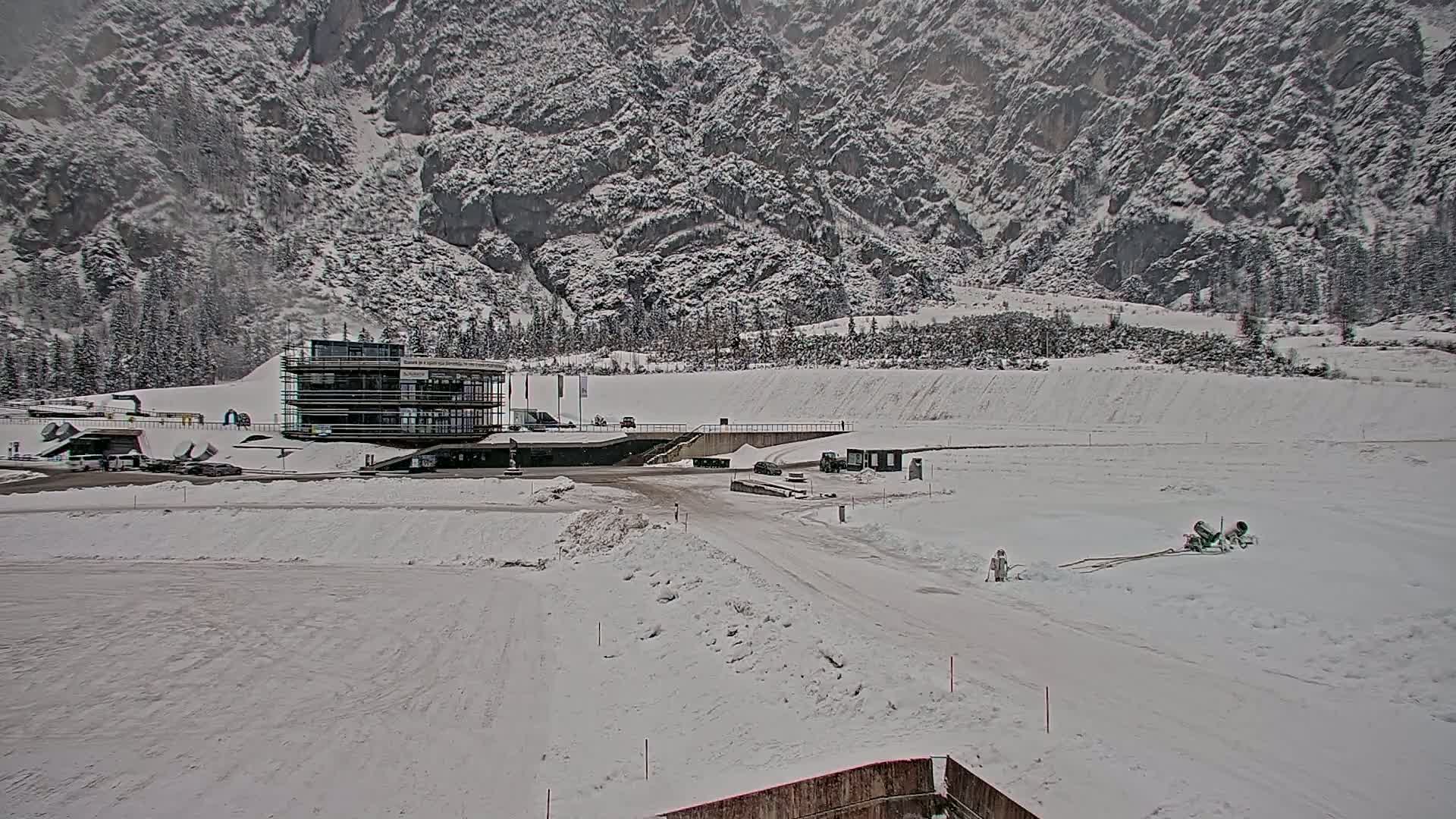 A snow-covered landscape features a modern building near a wide, snow-covered road, all set against a backdrop of snow-laden mountains.
