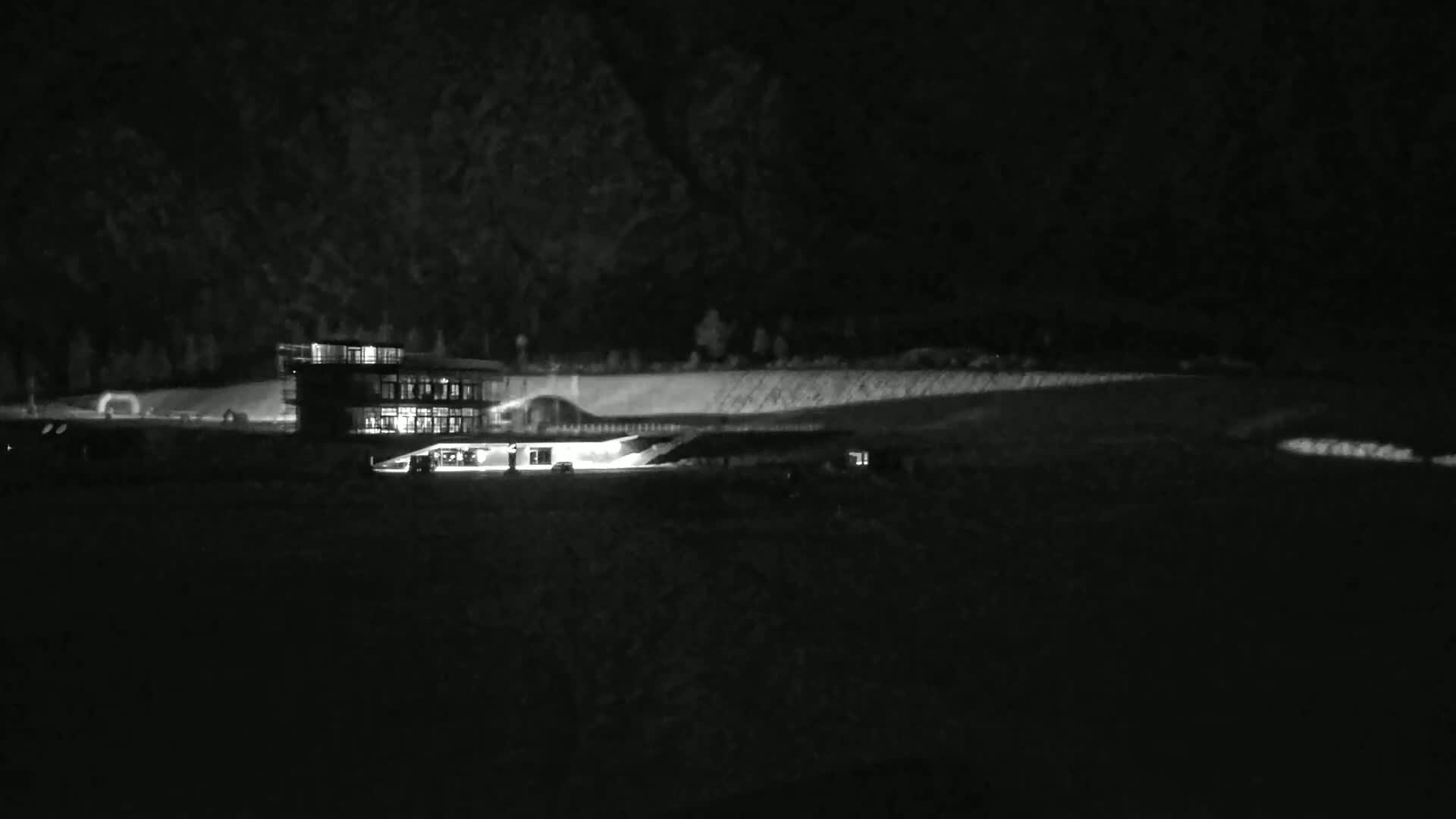 A lit building stands near a dark, snow-covered area at night.