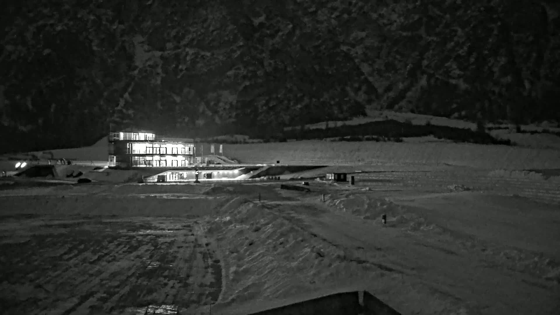 A multi-story building with illuminated windows sits on a snow-covered landscape at night, against a dark mountain backdrop.