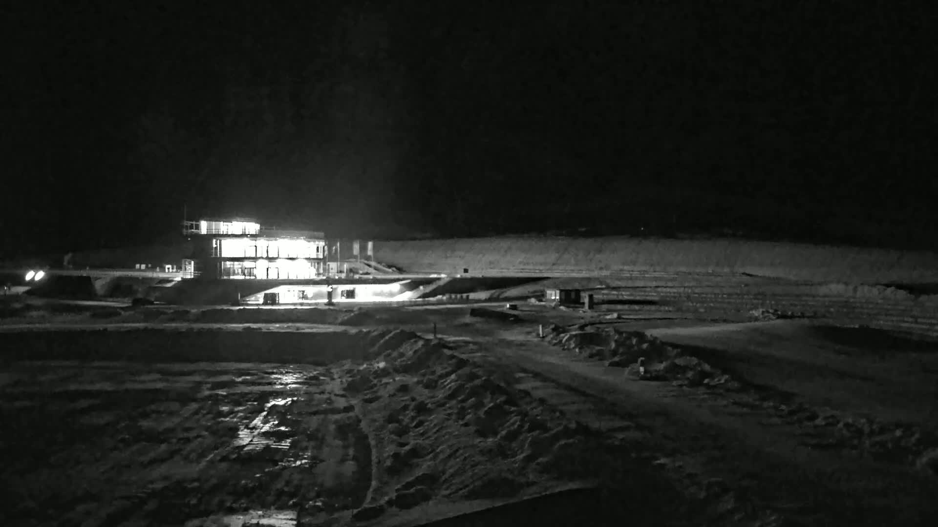 A brightly lit building stands in a snow-covered, dark nighttime landscape.